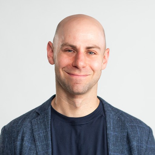 Adam Grant smiling in front of a white background.