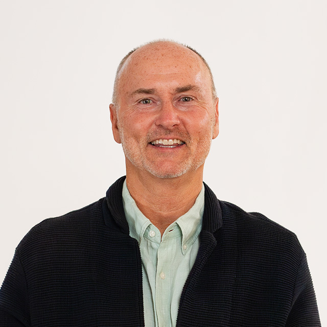 A bald man wearing a black jacket and green shirt.