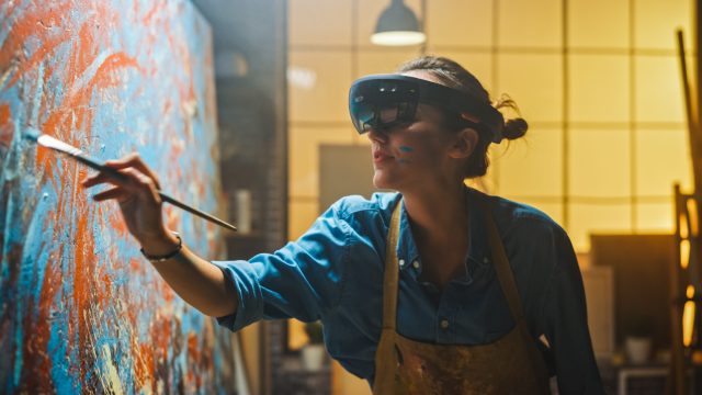 Artist wears augmented reality headset while working on abstract painting,