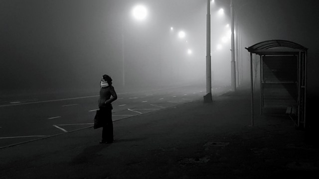 A woman waiting on an empty foggy street illustrating the concept of uncertainty.