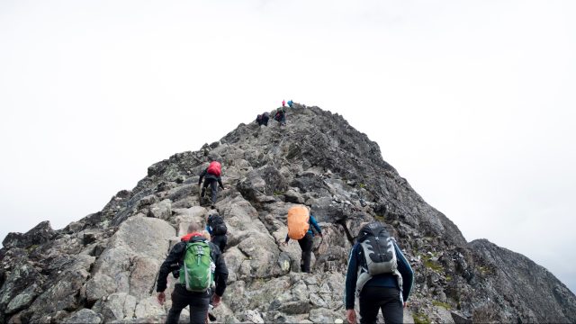 People climbing up a mountain following a leader