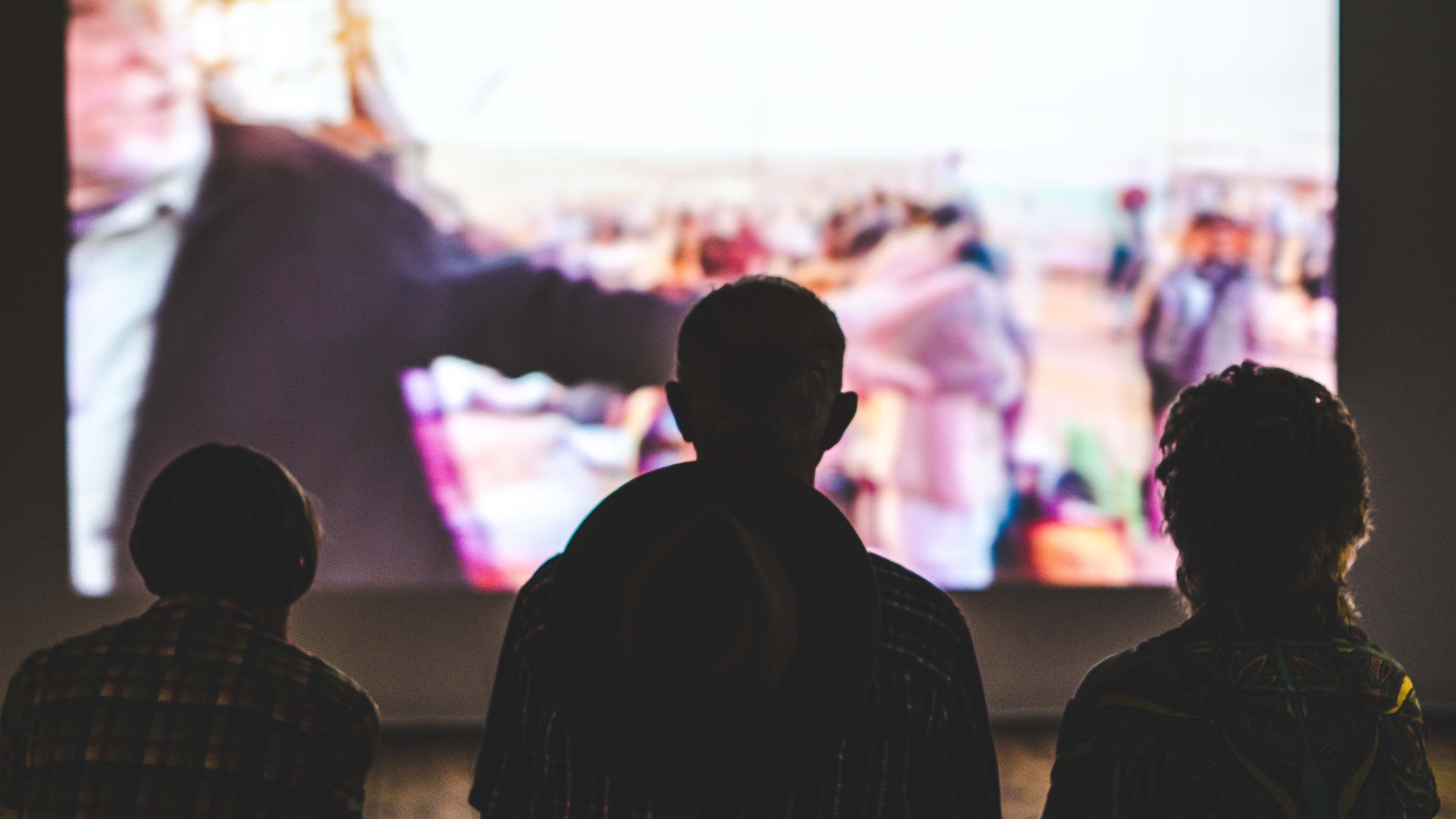 Silhouettes of three people watching a screen.