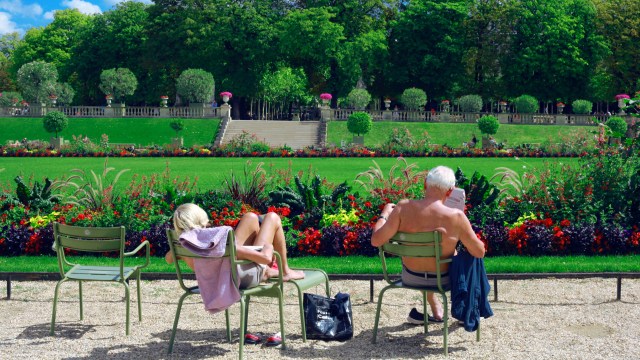 An older man and woman sunbathing in garden chairs.