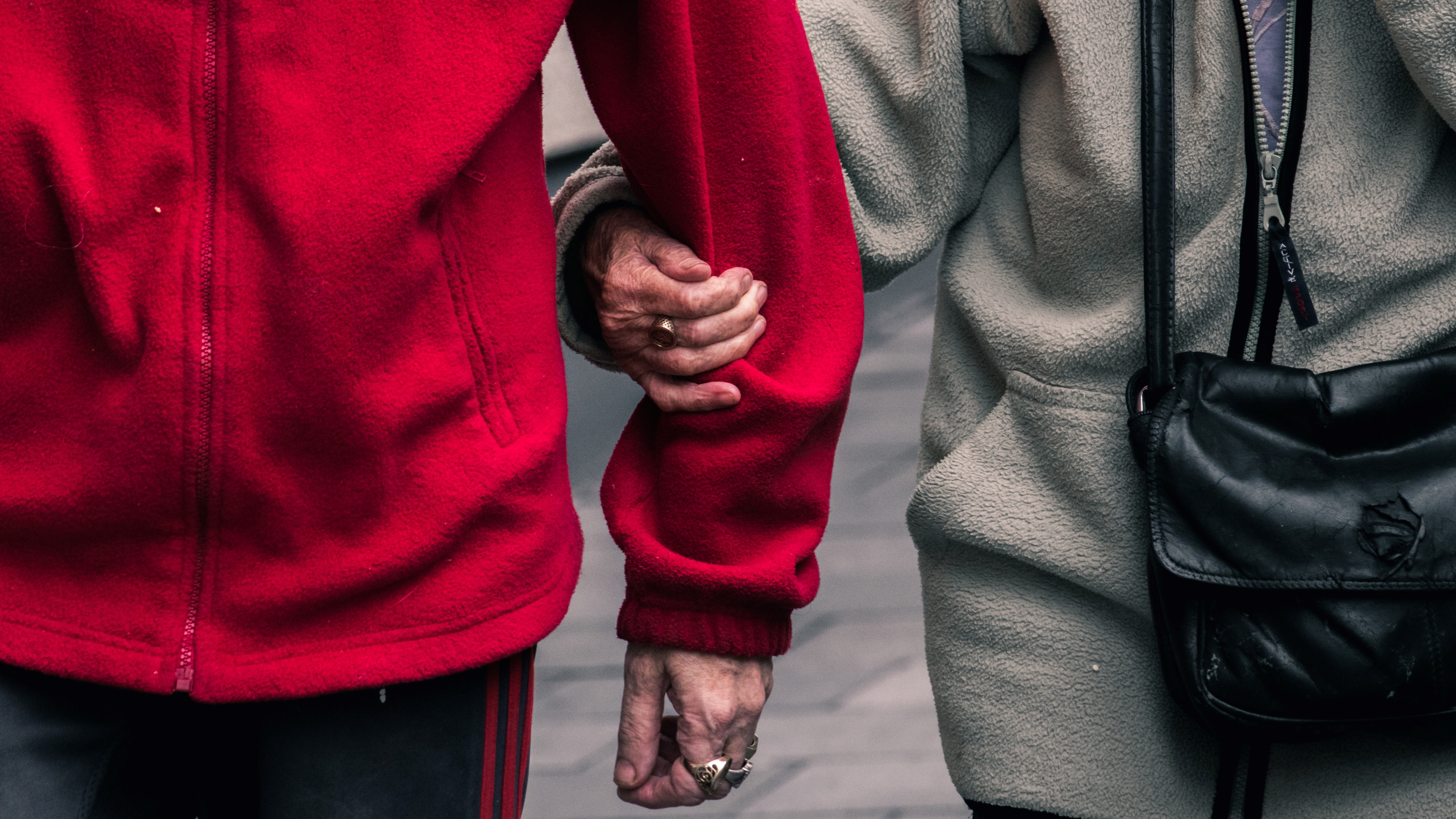 Two older adults linking arms while walking.