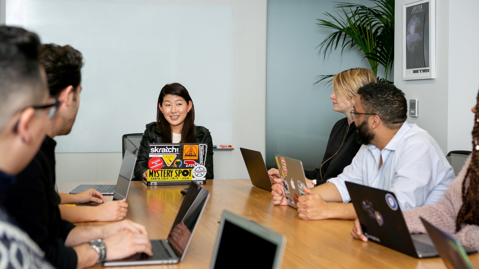 People sitting at a boardroom table with laptops.