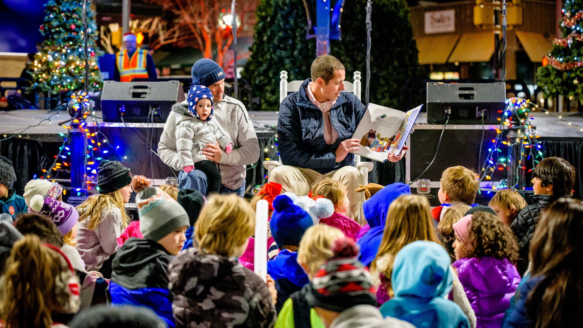 Two men read a book to a crowd of children during the Christmas season.