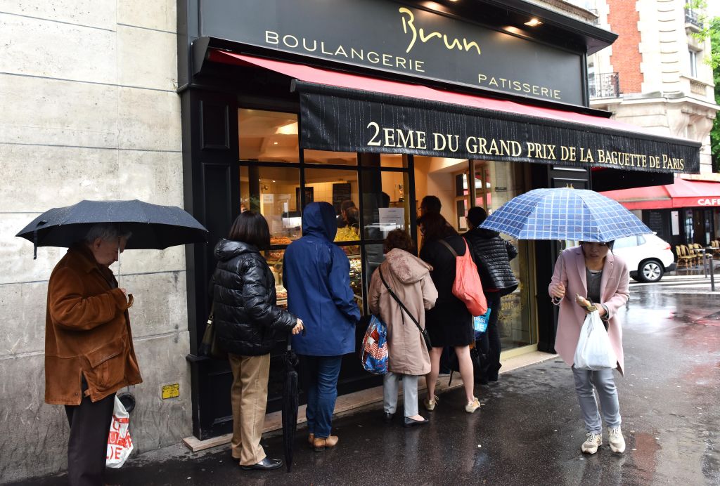 People standing in line outside a shop with umbrellas