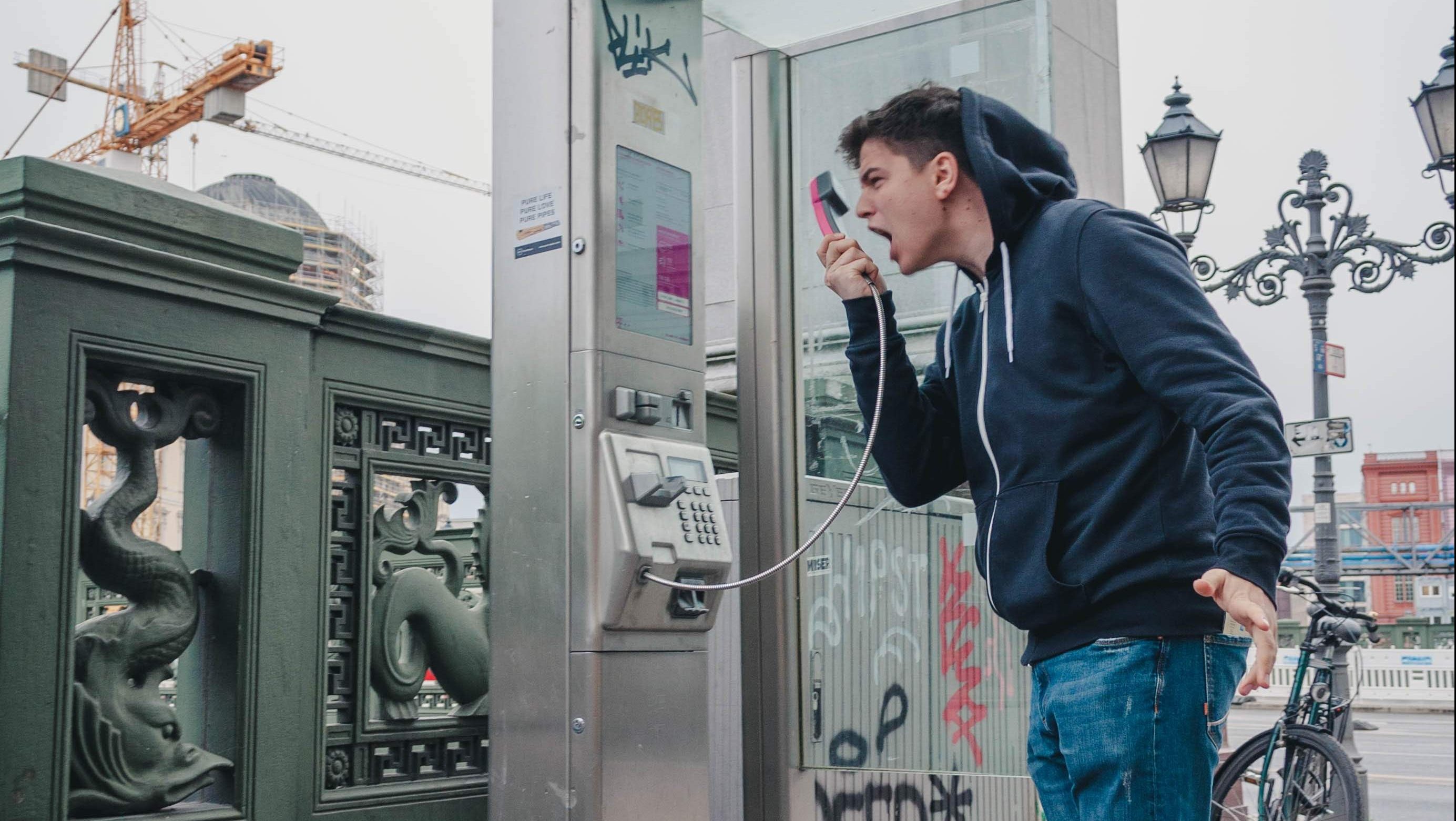 a man yelling into a receiver of a phone booth