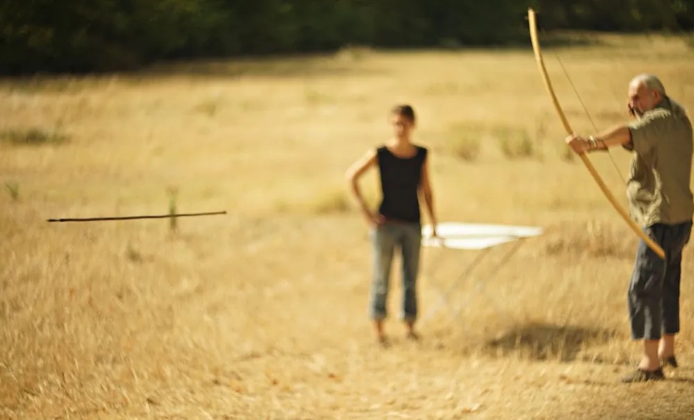 a man and a woman standing in a field with a bow and arrow.