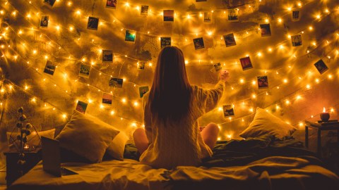 a woman sitting on a bed in front of a string of lights.