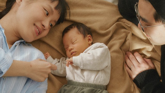 A man and woman laying on a bed with a baby.