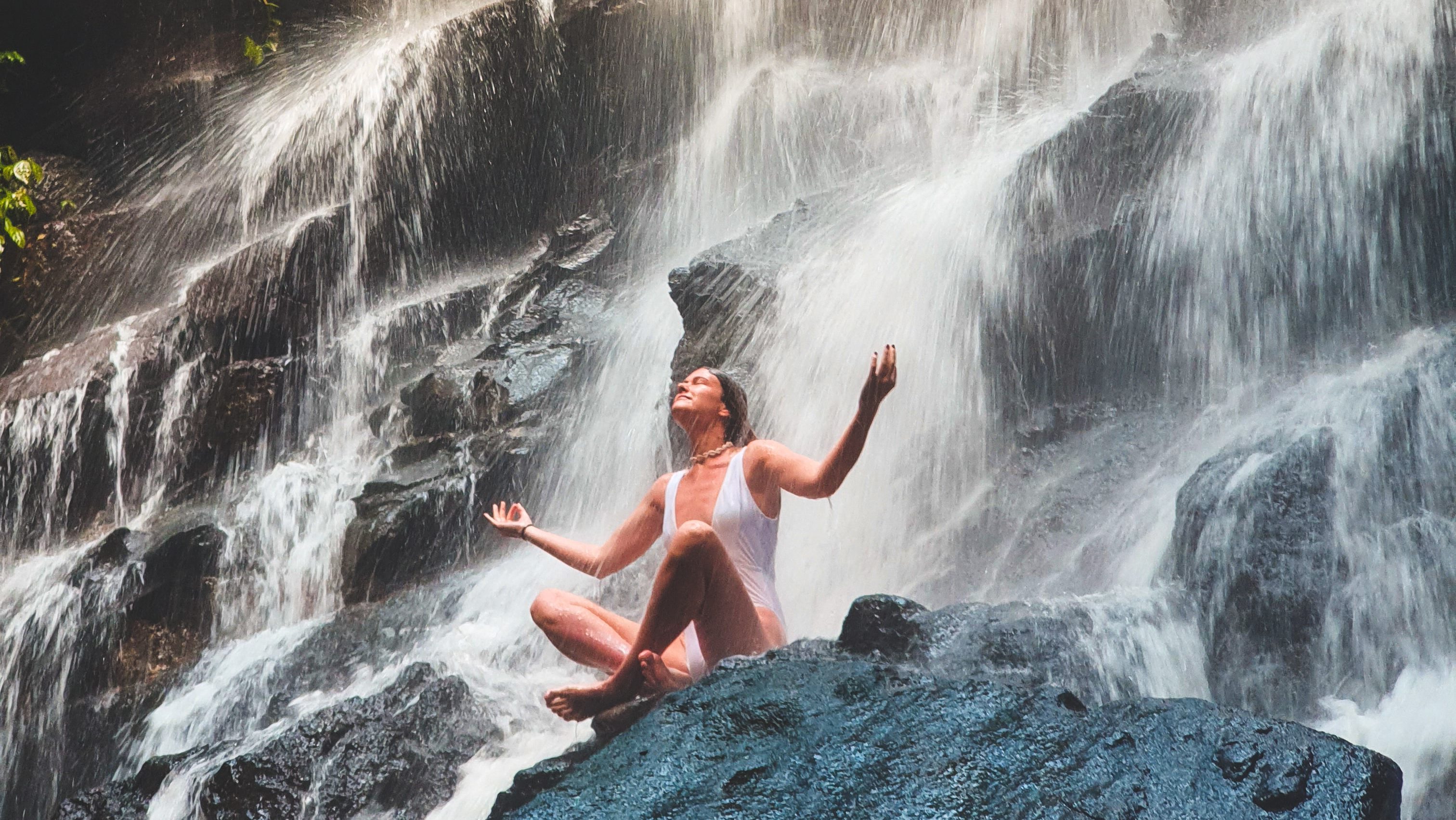 A woman sitting on a rock in front of a waterfall.