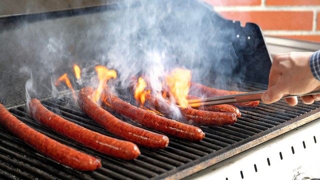 a person cooking hot dogs on a grill.