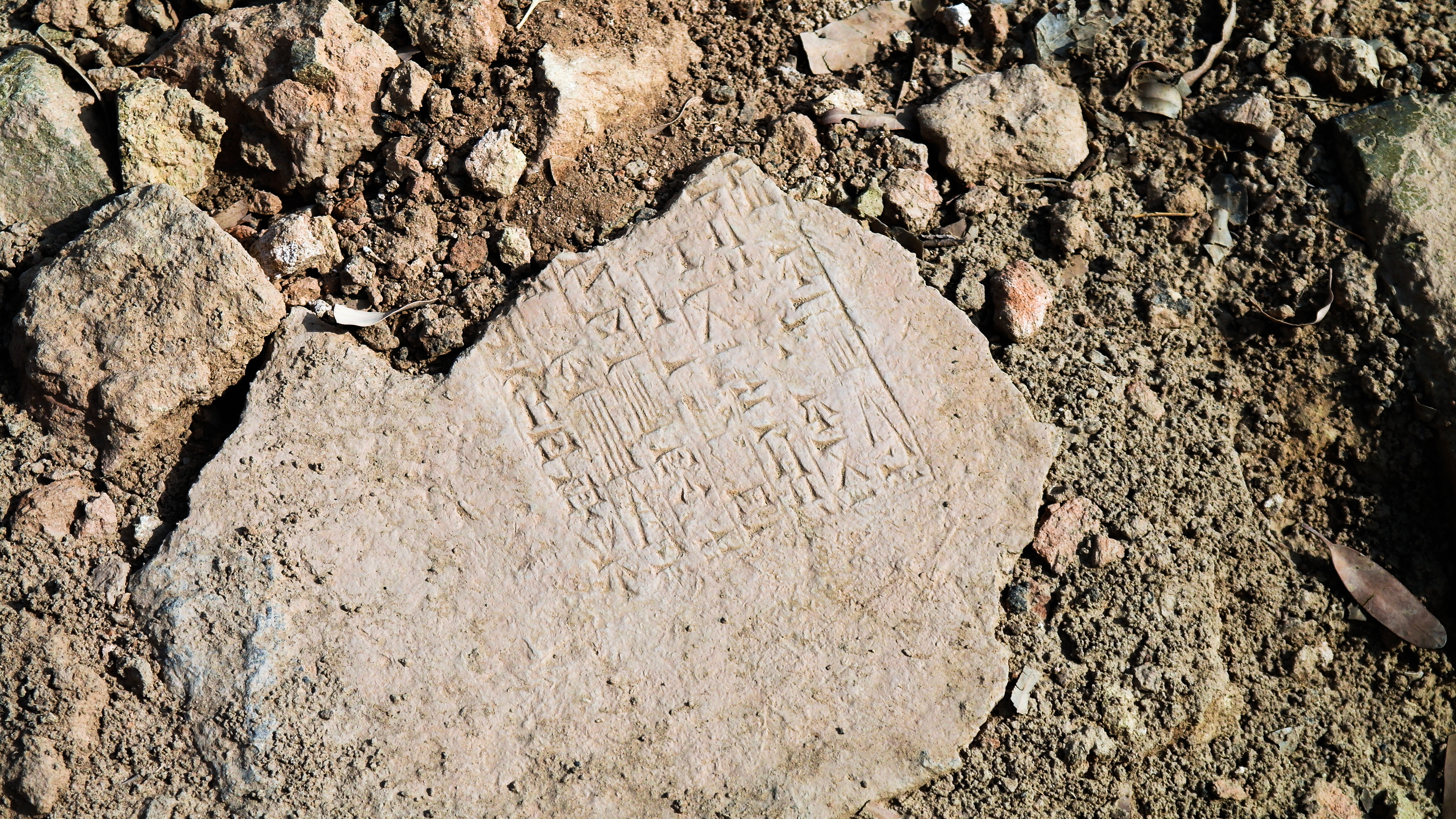 A stone with cuneiform writing laying on the ground.