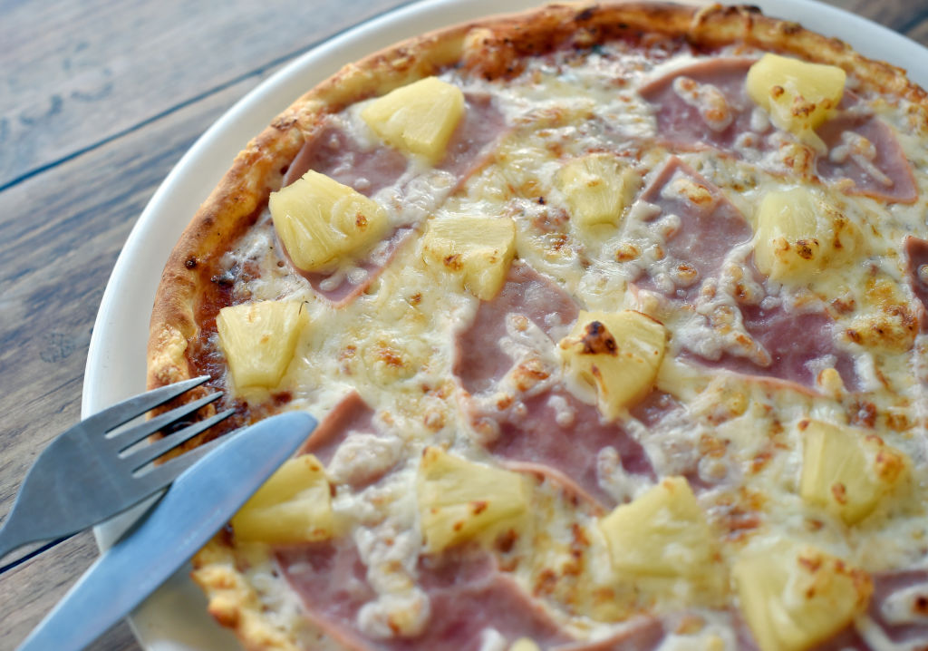 A pizza with pineapple and ham on a white plate.