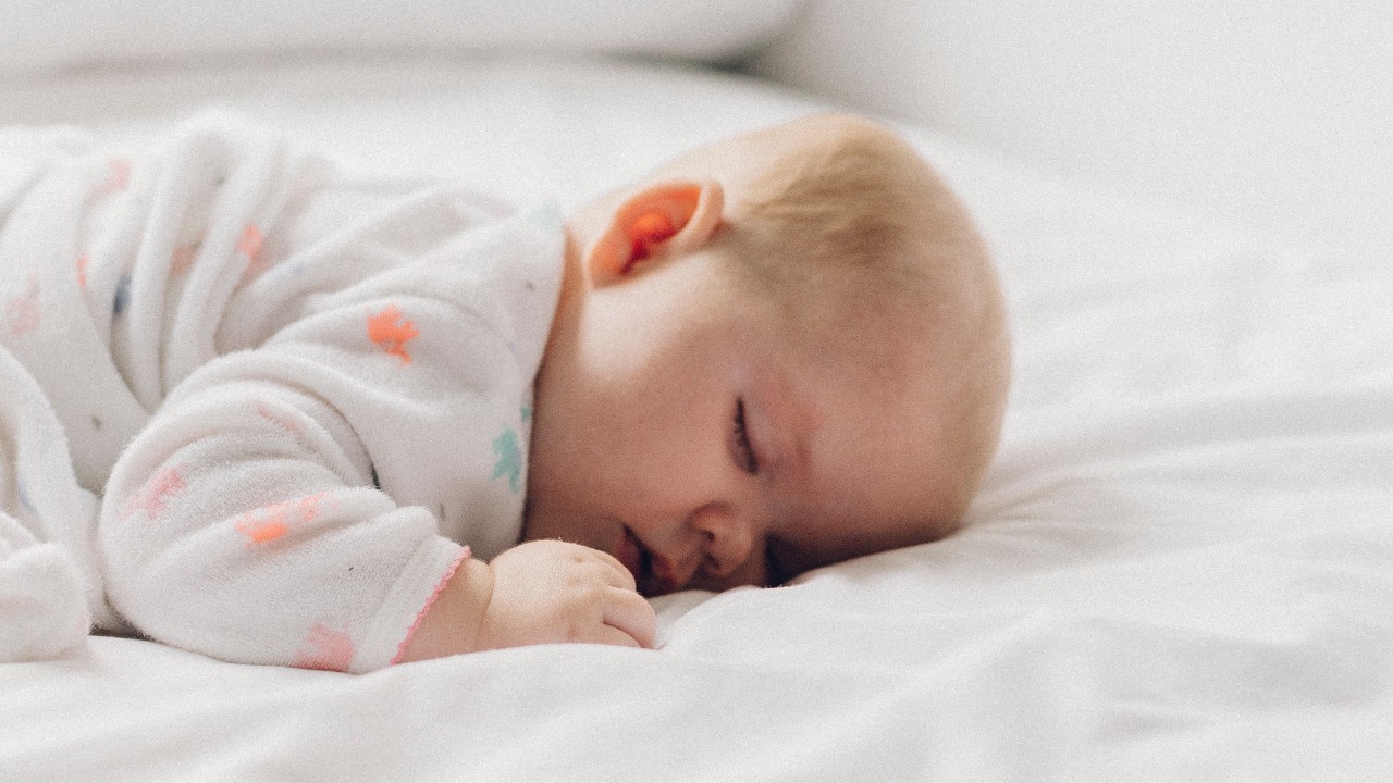 A baby is sleeping on a white bed.