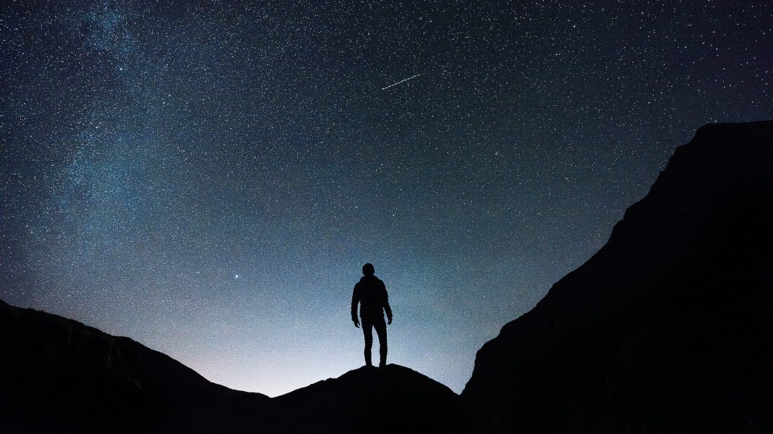 a person standing on top of a mountain under a starry sky.