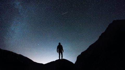 a person standing on top of a mountain under a starry sky.