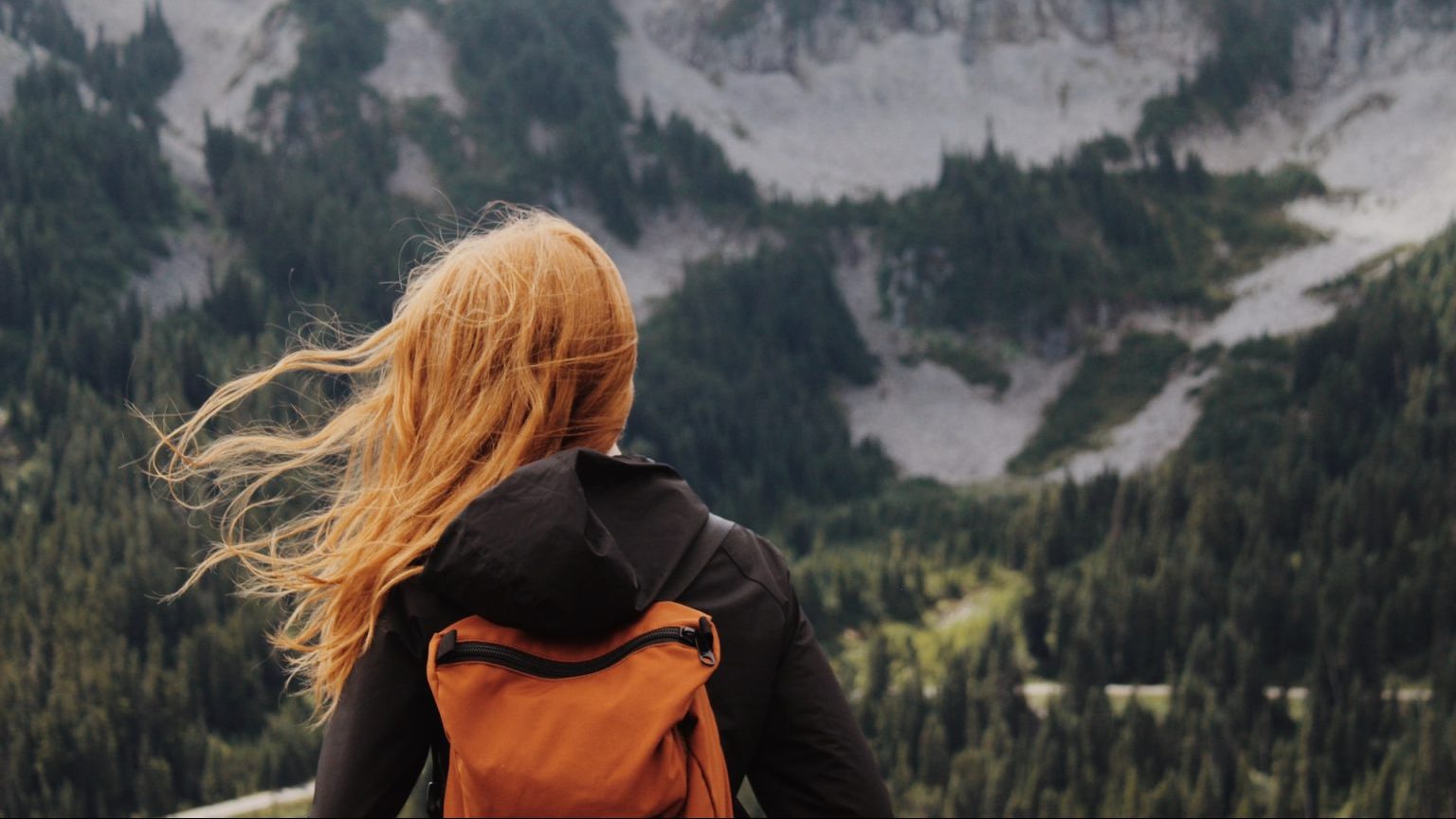 a woman with a backpack looking at the mountains.