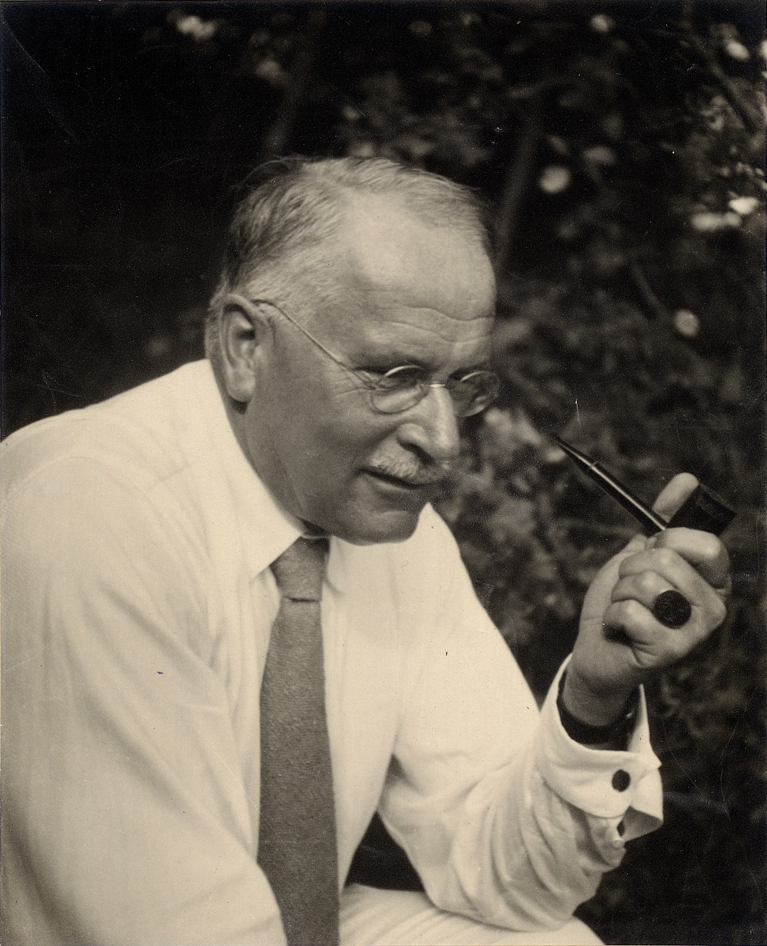 a man in a white shirt and tie embodying Carl Jung while smoking a pipe.