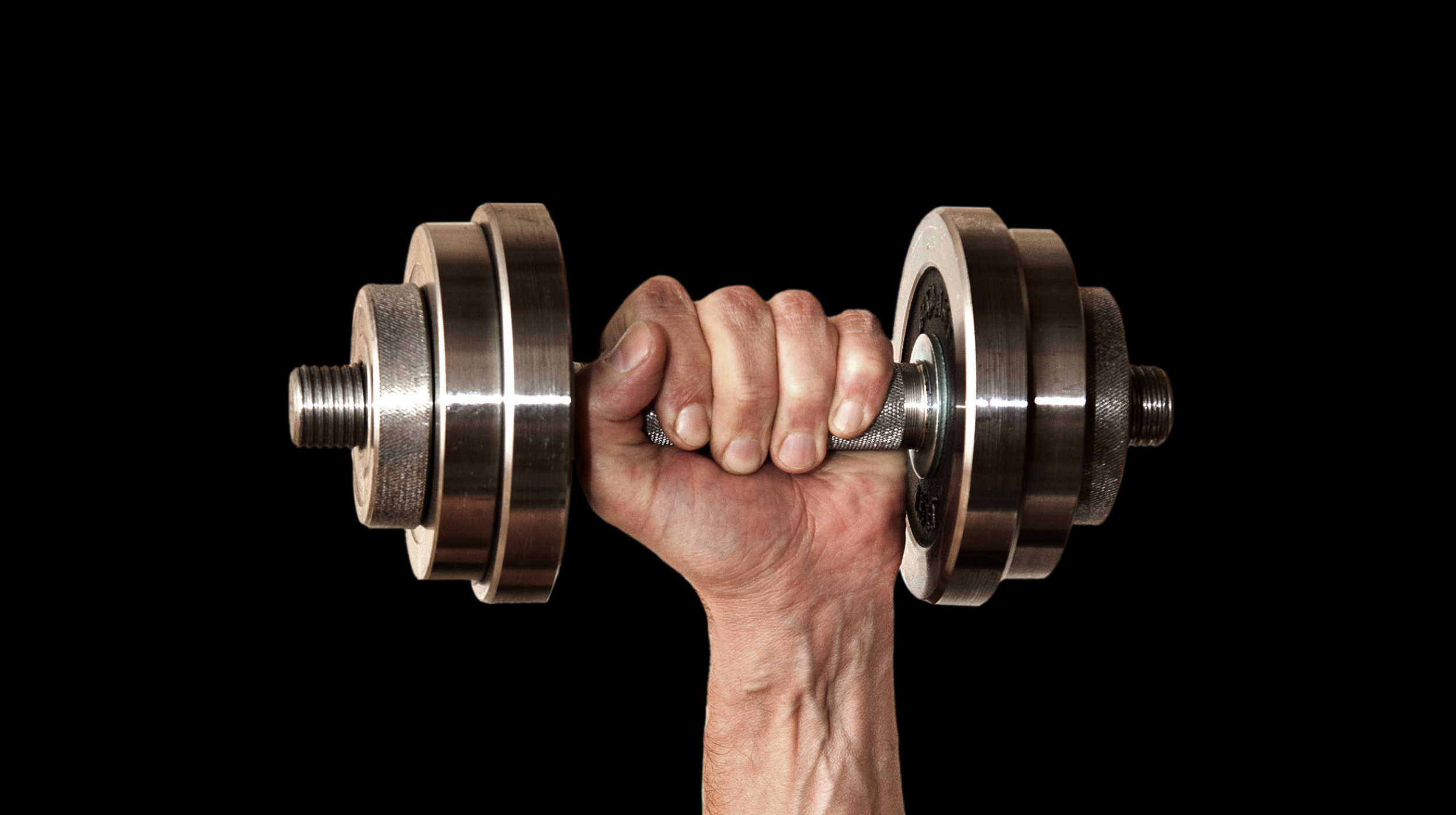 A man's hand holding a pair of dumbbells on a black background.