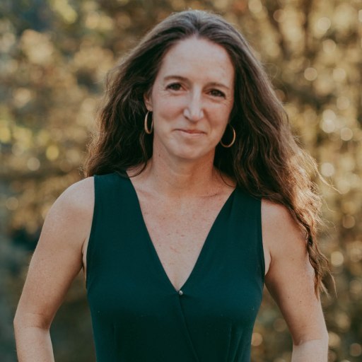 A woman in a green dress standing in front of trees.