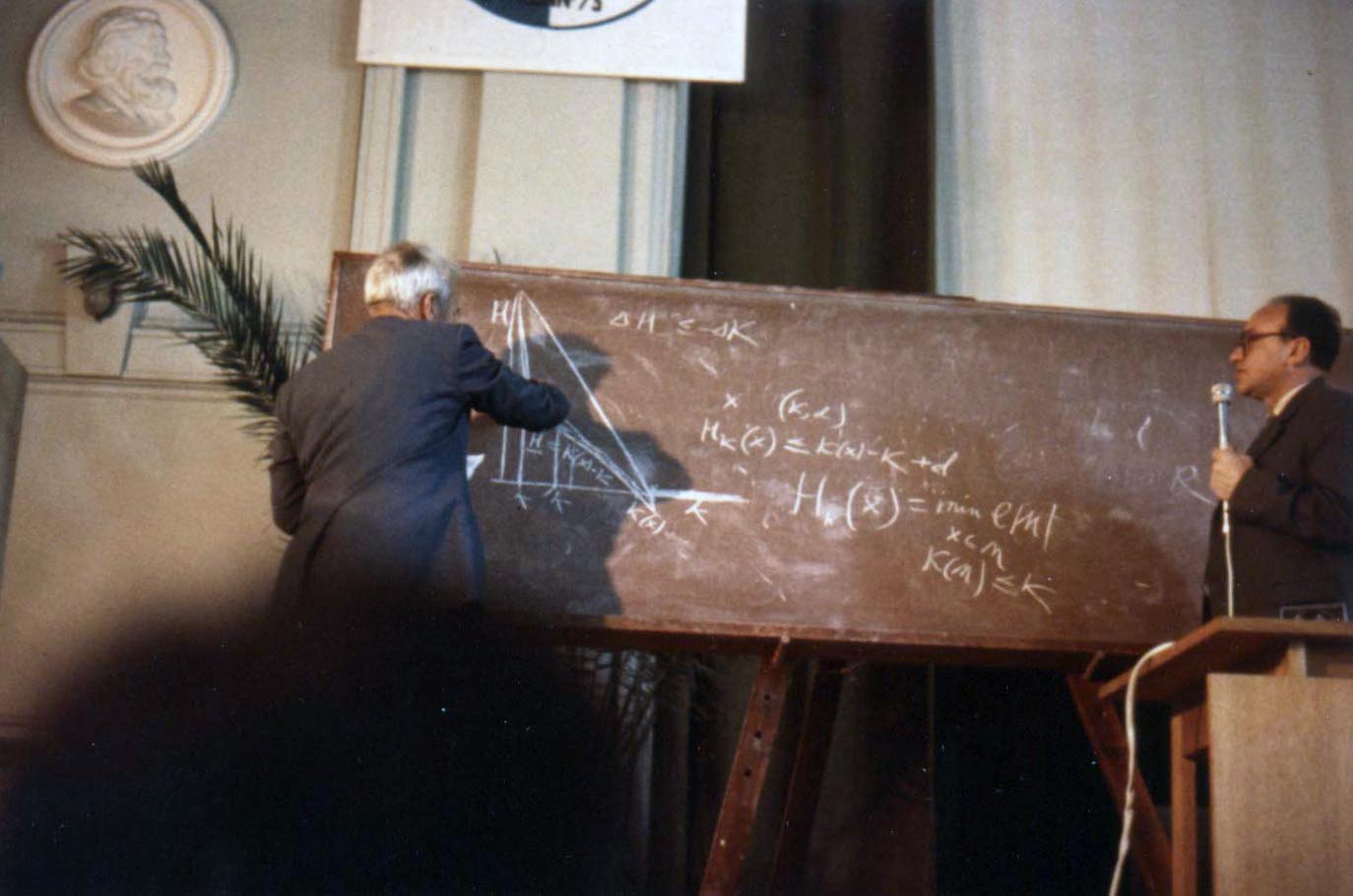 Two men standing in front of a blackboard.