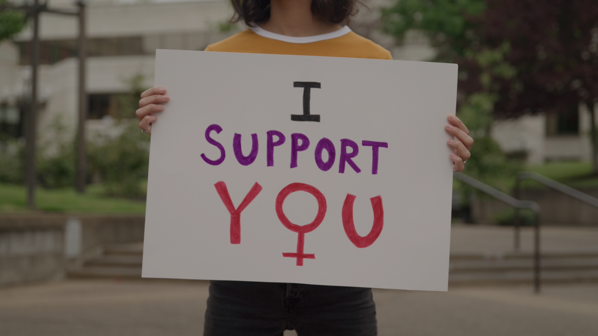 A woman holding up a sign that says i support you.
