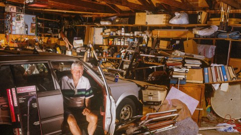 A man displaying signs of hoarding disorder, sitting in a car in a garage.