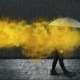 A person is walking with an umbrella in front of a yellow smoke.