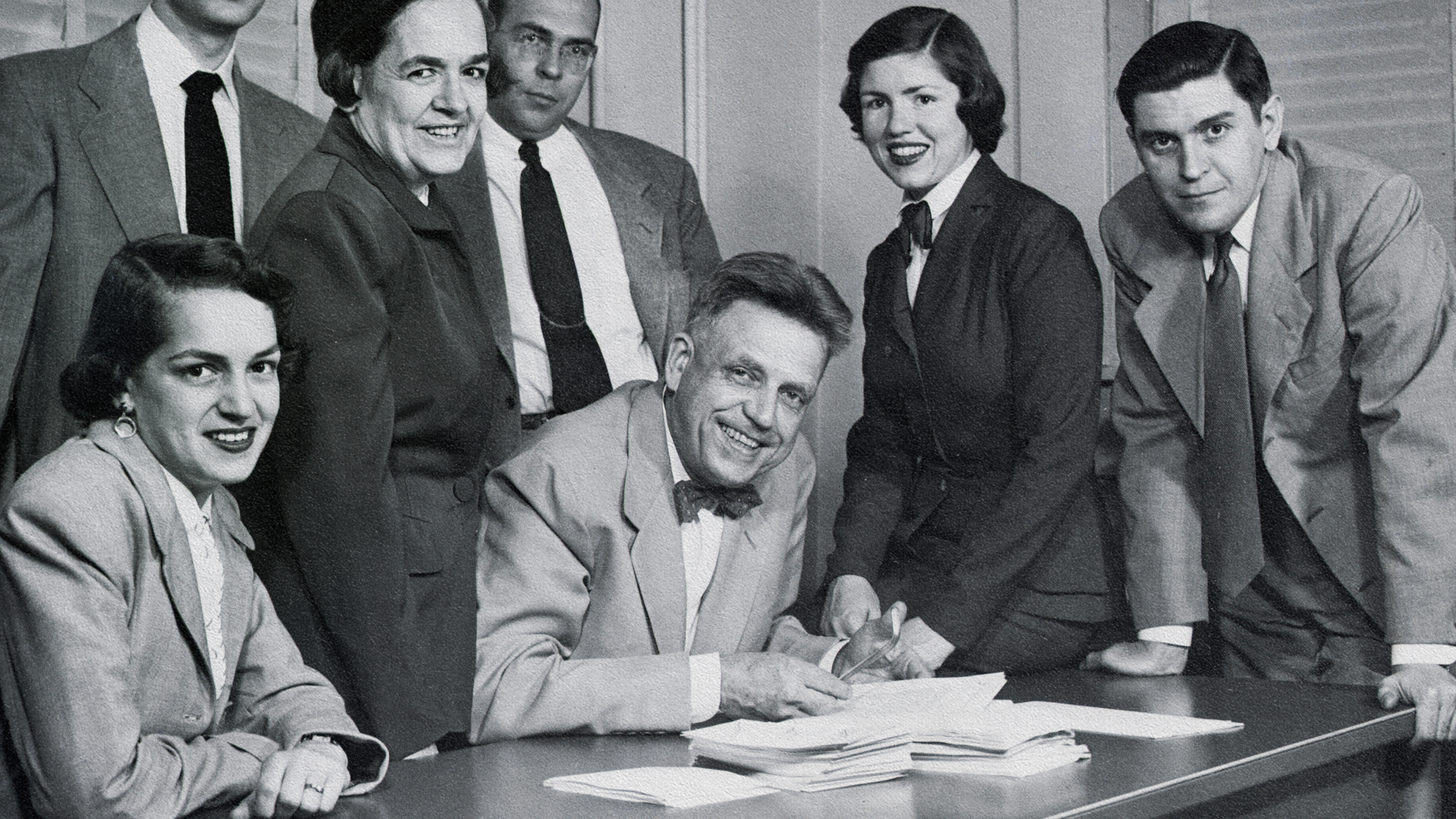 A group of people sitting around a desk signing papers during a Kinsey study.
