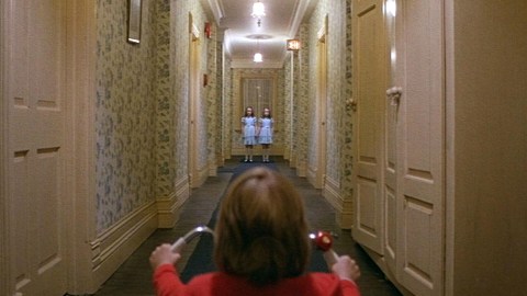 A girl is walking down a hallway in a red shirt, feeling fear.