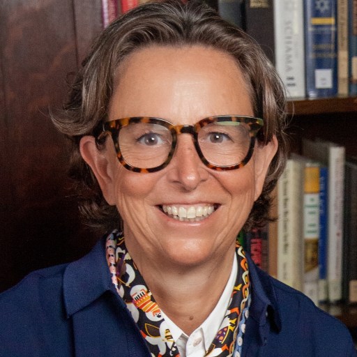 A woman in glasses is smiling in front of a bookcase.