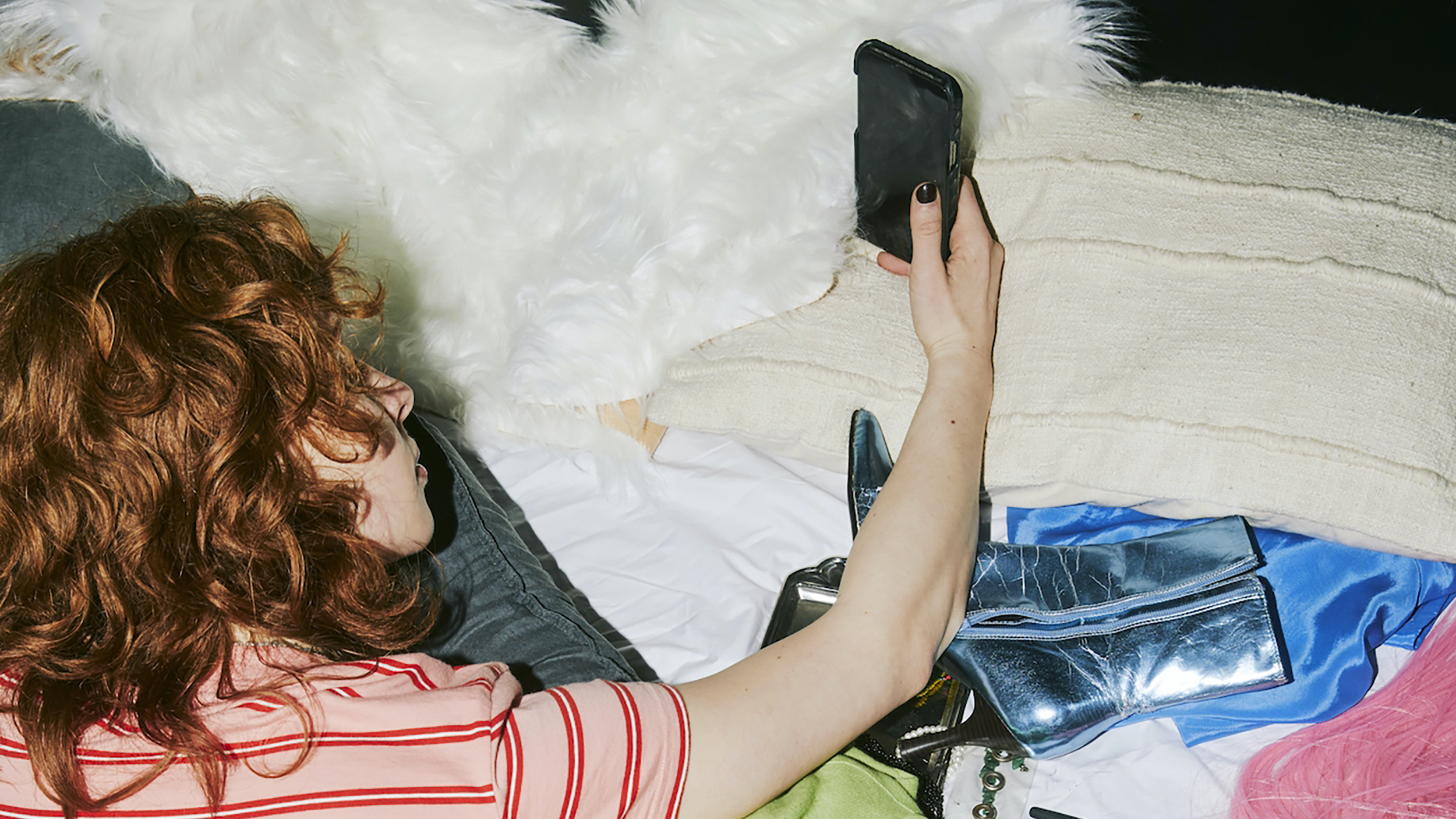 A Gen Z woman reshuffling on a bed with a cell phone.