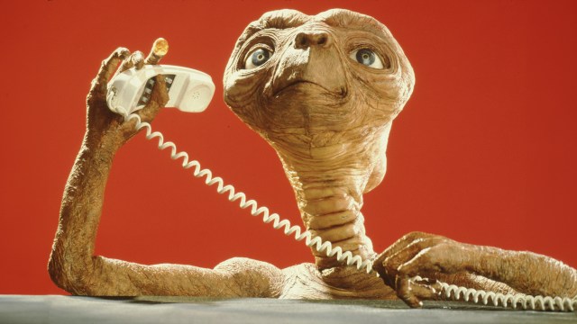 A little alien talking on a telephone.