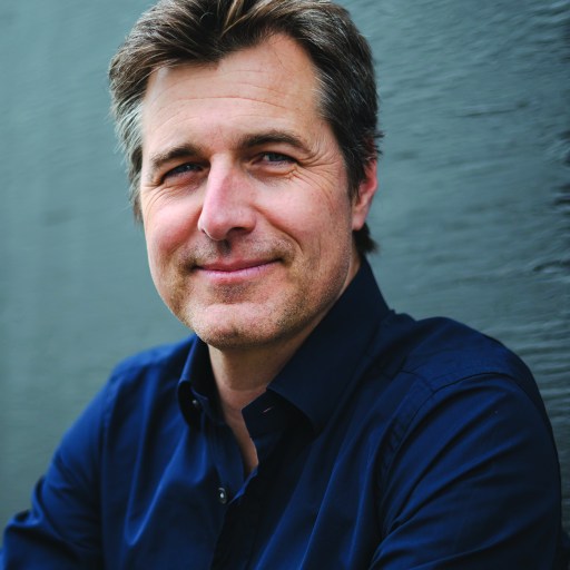 A man in a blue shirt leaning against a wall.