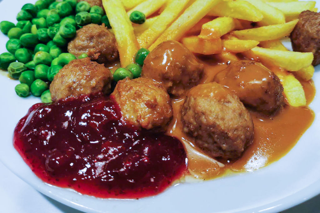 A plate with meatballs, peas and fries.