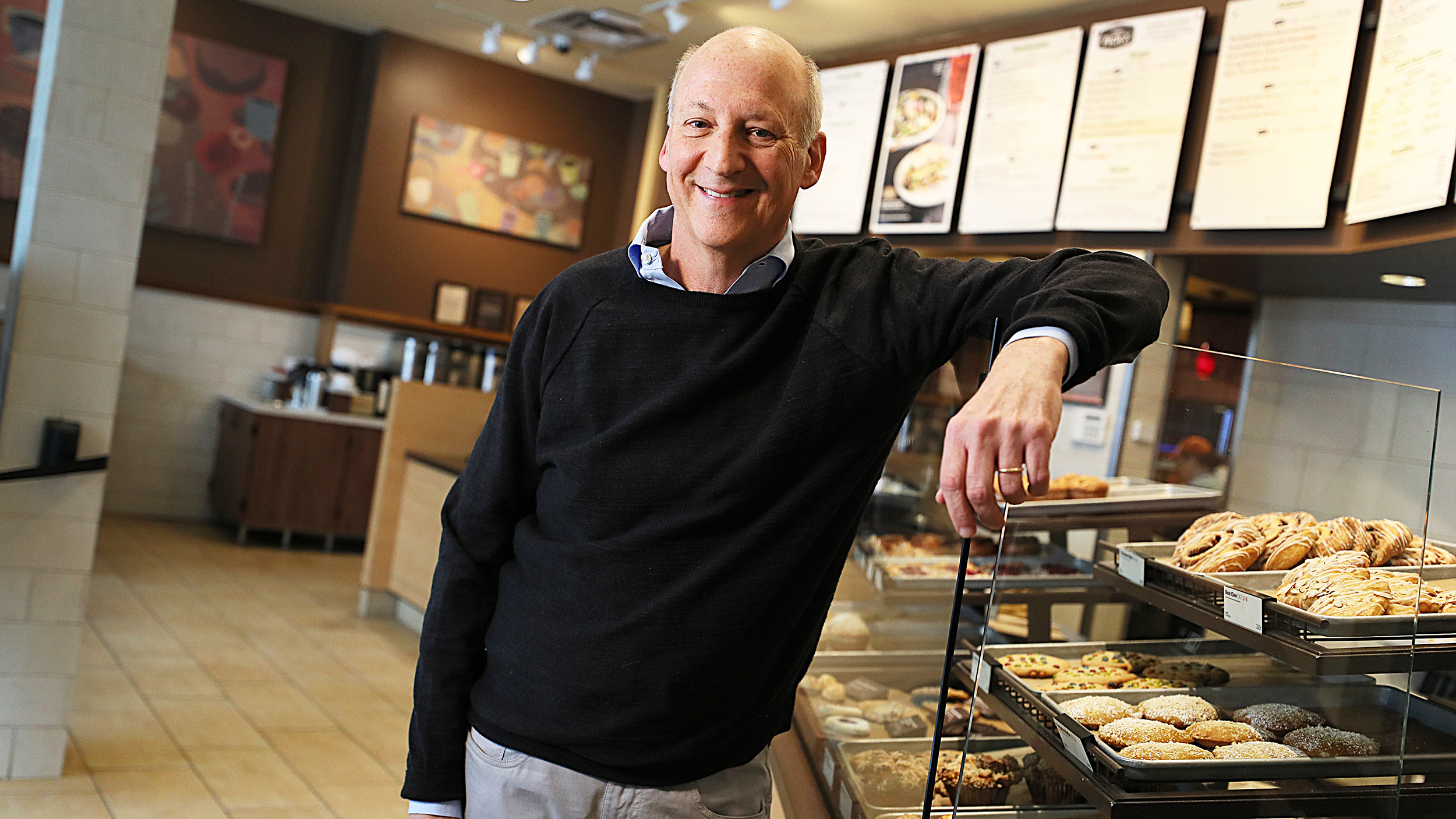 A man standing in front of a display of pastries at Panera Bread.