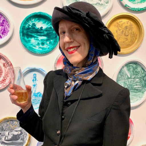 A woman holding a glass of wine in front of a wall of plates.