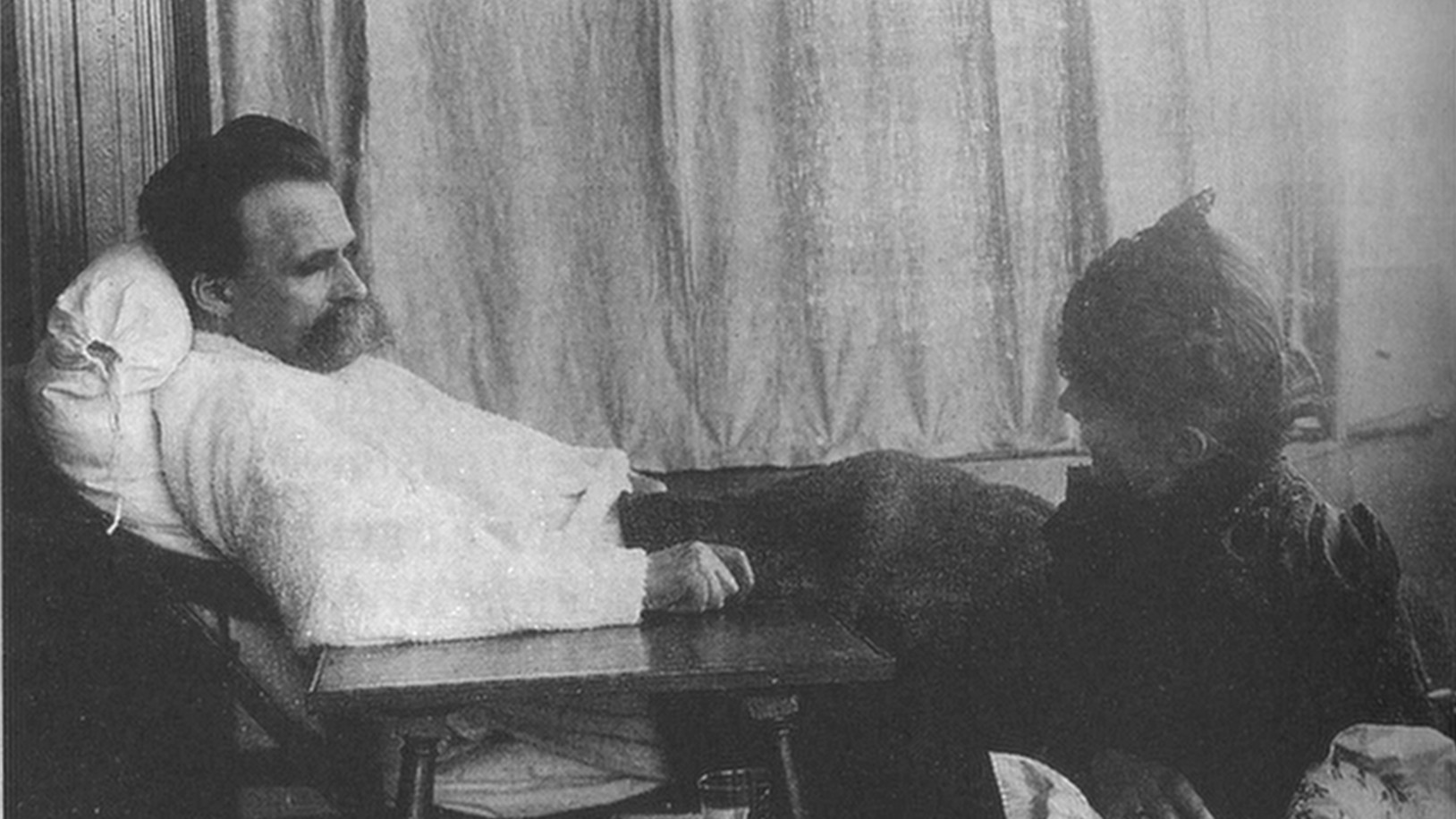 A man sitting in a chair next to a woman, pondering Friedrich Nietzsche's philosophy.