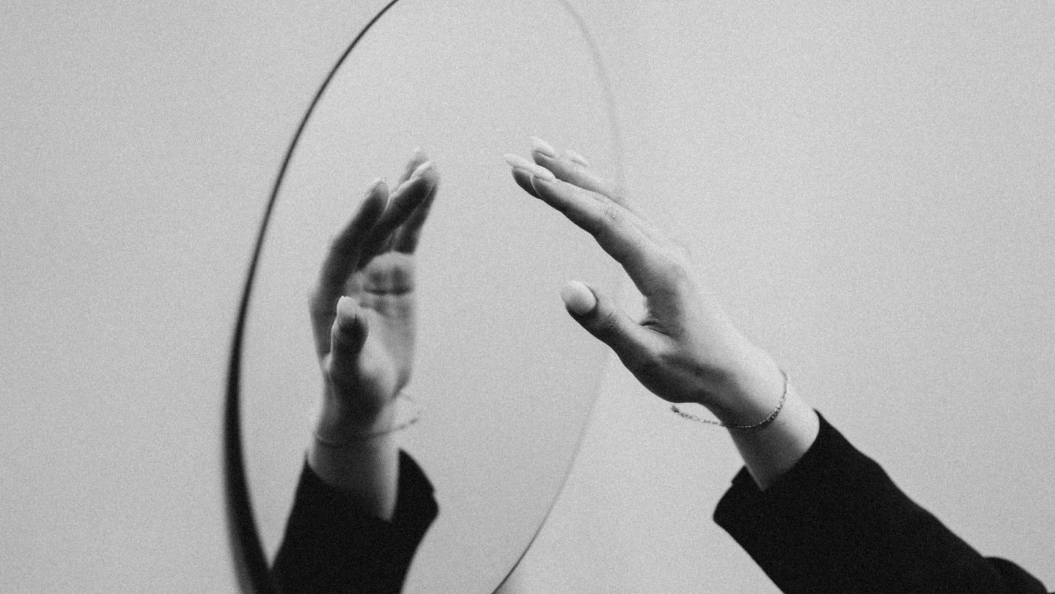 A black and white photo of a hand reaching into a mirror.