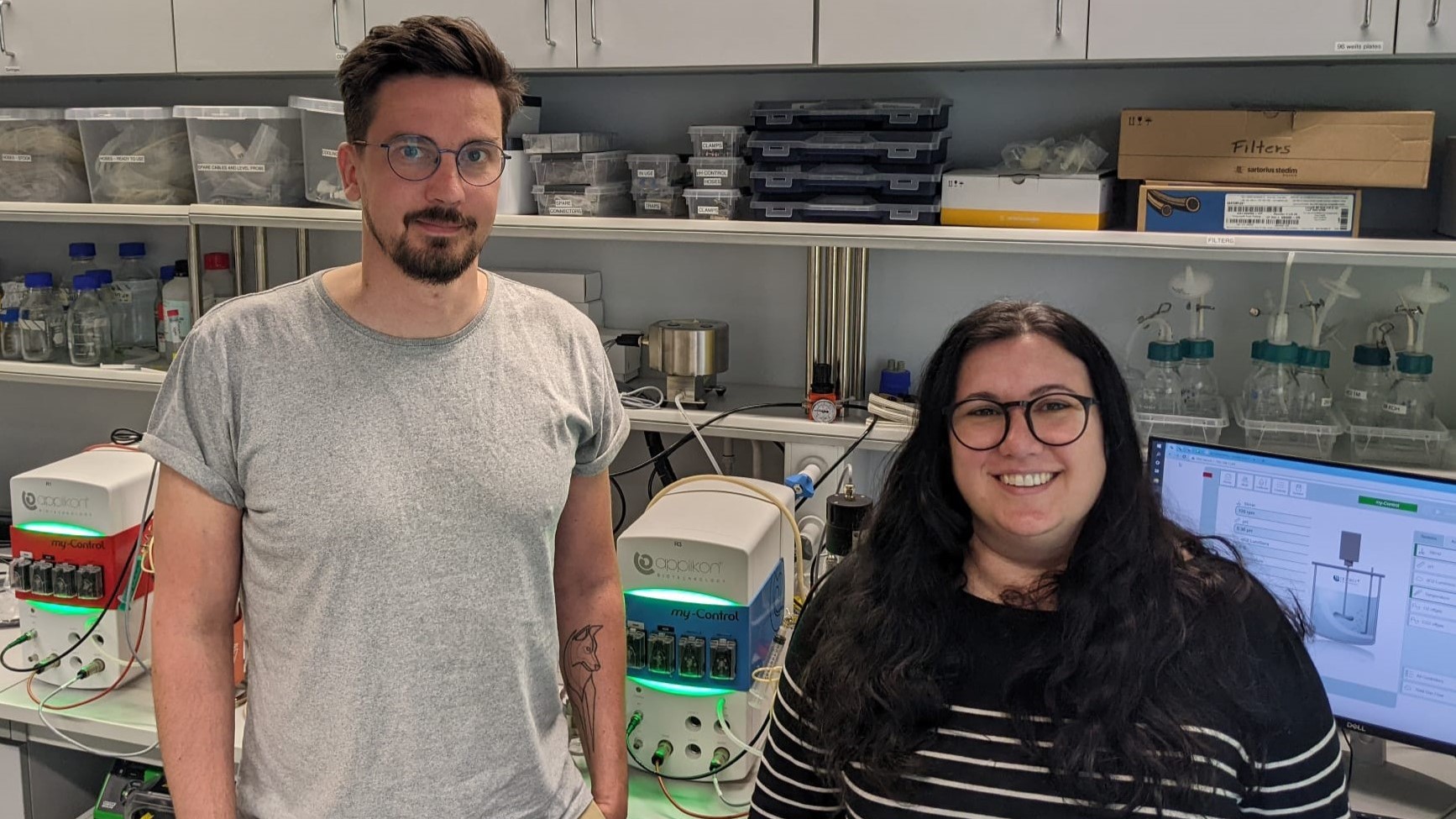 Two people standing in front of a lab with a lot of equipment.