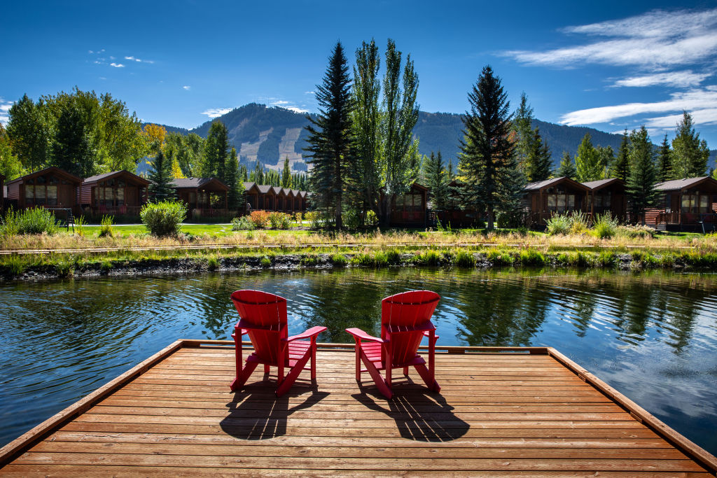Two red chairs sit on a dock overlooking a lake.
