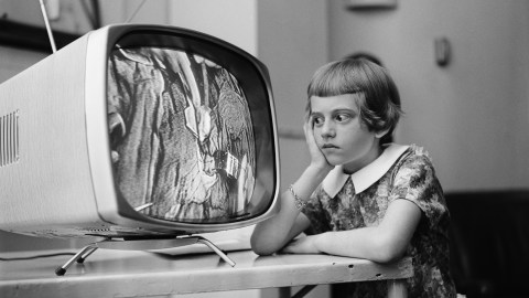A young girl giving her undivided attention to a TV screen displaying an engaging cartoon.