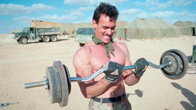 A man showcasing his strength by lifting a barbell in the barren desert.