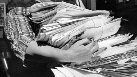 Black and white photo of a woman holding a stack of papers, illustrating Parkinson's Law.