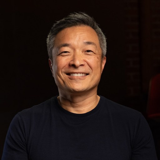 An asian man smiling in front of a black background.