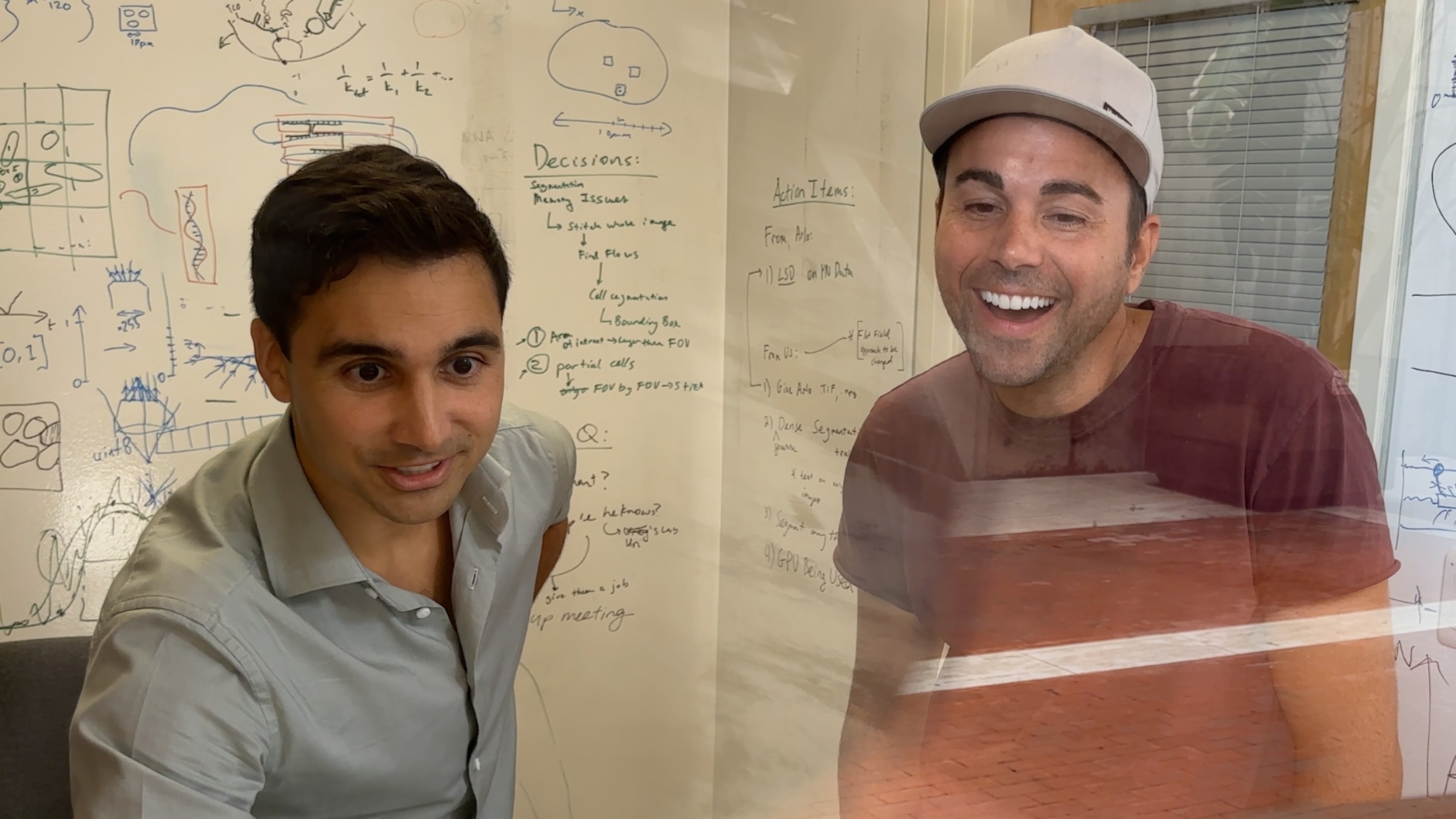 Two men smiling in front of a white board.