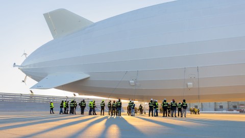 A group of people standing in front of a large white blimp.