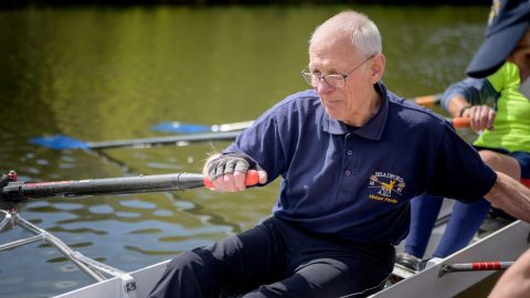 An aging man is rowing in a rowing boat, showcasing his strength despite potential muscle loss.